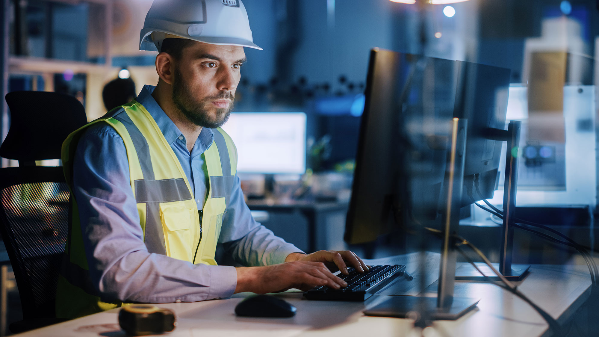 male-engineer-wearing-safety-vest-working-at-computer