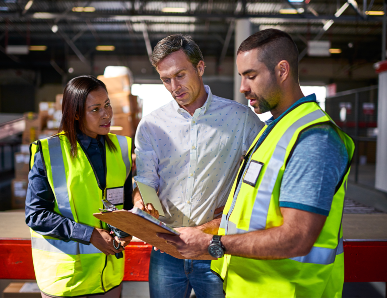 three-workers-at-a-worksite-looking-at-a-clipboard