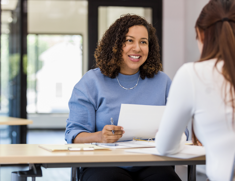 woman-holding-document-and-smiling-at-another-woman-across-from-her