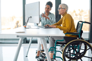 two employees having a conversation at a computer, one person in a wheelchair