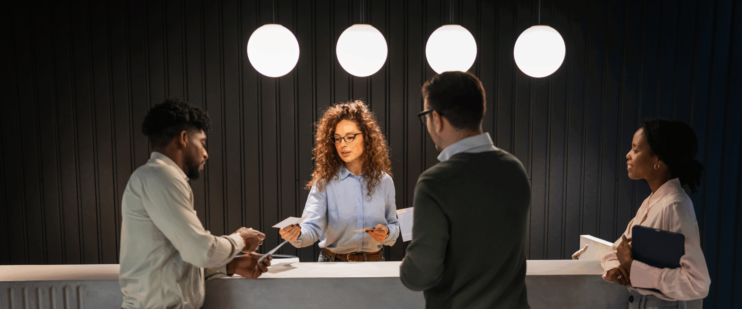 People interacting with a smiling woman at reception desk
