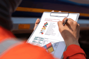An engineer is checking on chemical hazardous material checklist to verify the safety condition with chemical road tanker as background. Industrial waorking scene, close-up and selective