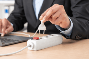 Close up of man hand plugging plug on a power strip socket using laptop on a desk at office