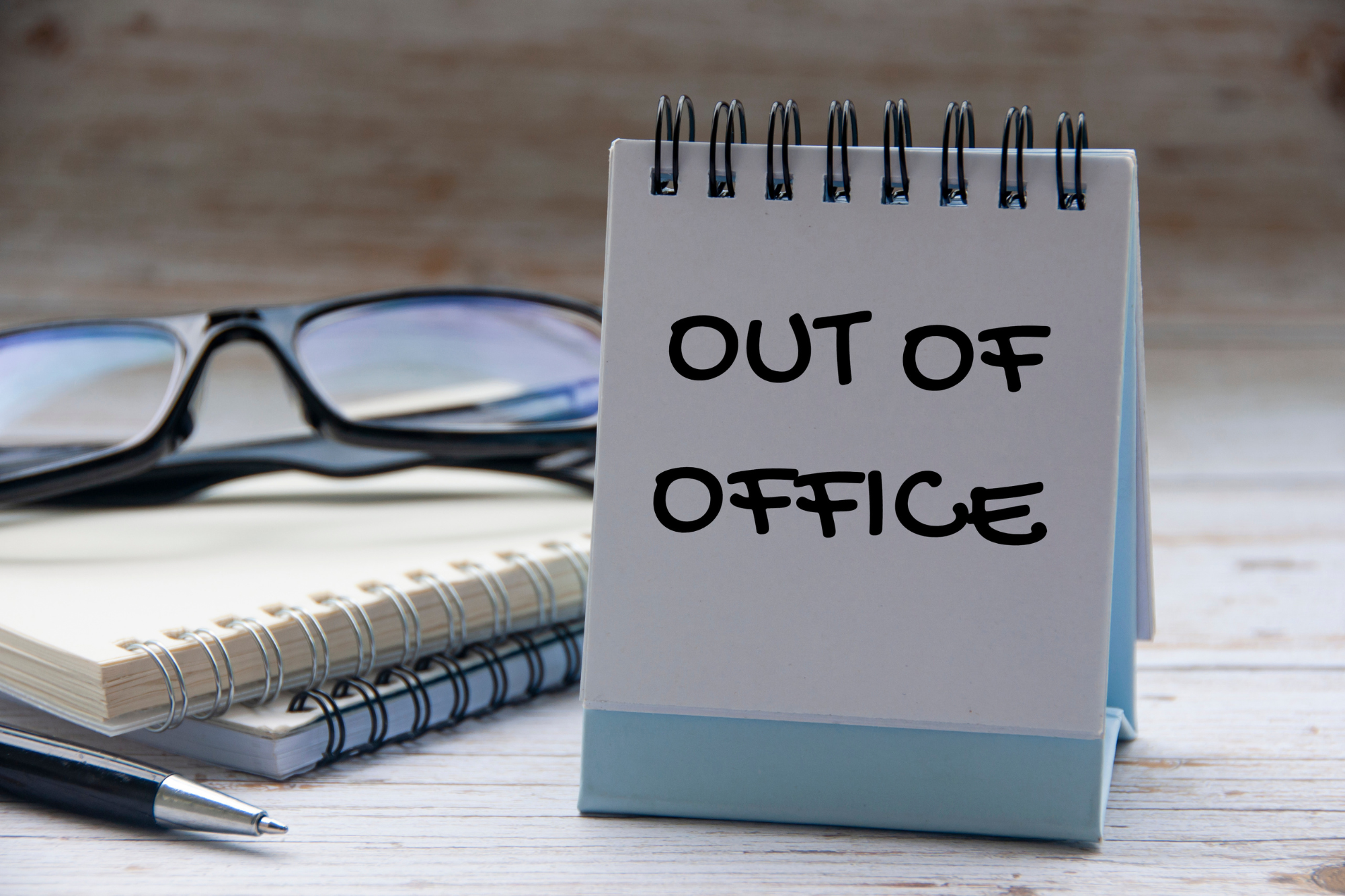 Out of office text on calendar desk with notebook and glasses background.