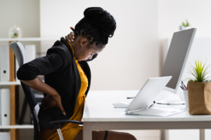 Employee experiencing lower back pain while sitting at a workstation with poor posture, illustrating common ergonomic risks in the workplace.