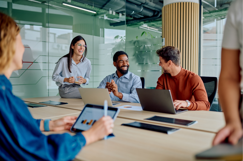 Diverse group of business professionals collaborating in a team meeting, sharing ideas, smiling, and using digital technology to support workplace communication and employee engagement.