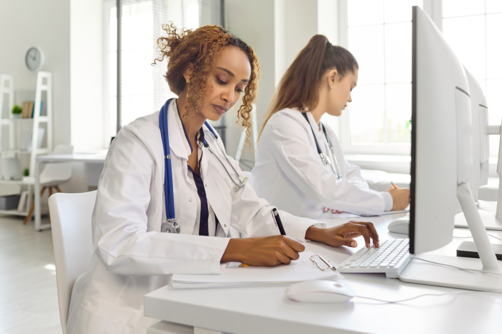 Healthcare professionals reviewing employee records and training documentation on computers in a medical office.