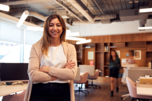 Portrait Of Smiling Businesswoman Standing In Busy Modern Open Plan Office